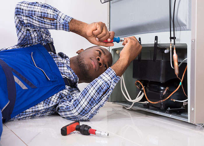 male serviceman working on fridge with screwdriver